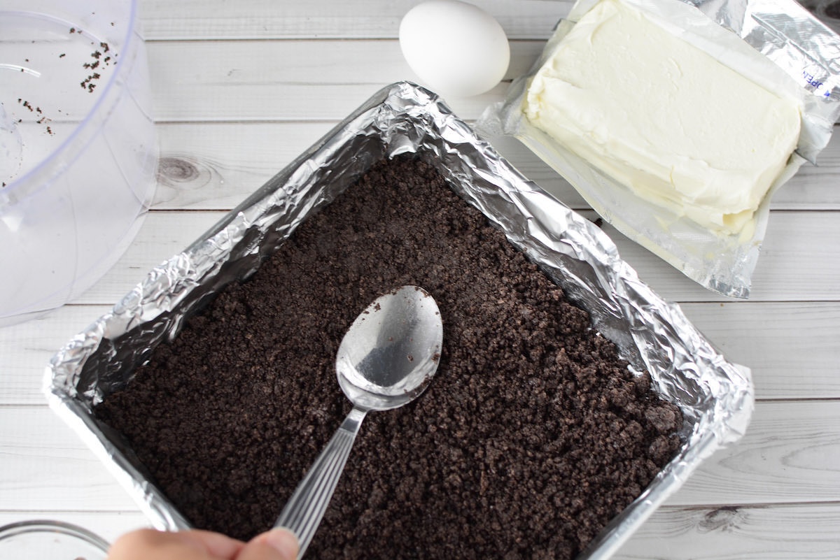 Mocha Oreo crumbs being pressed into the bottom of a pan