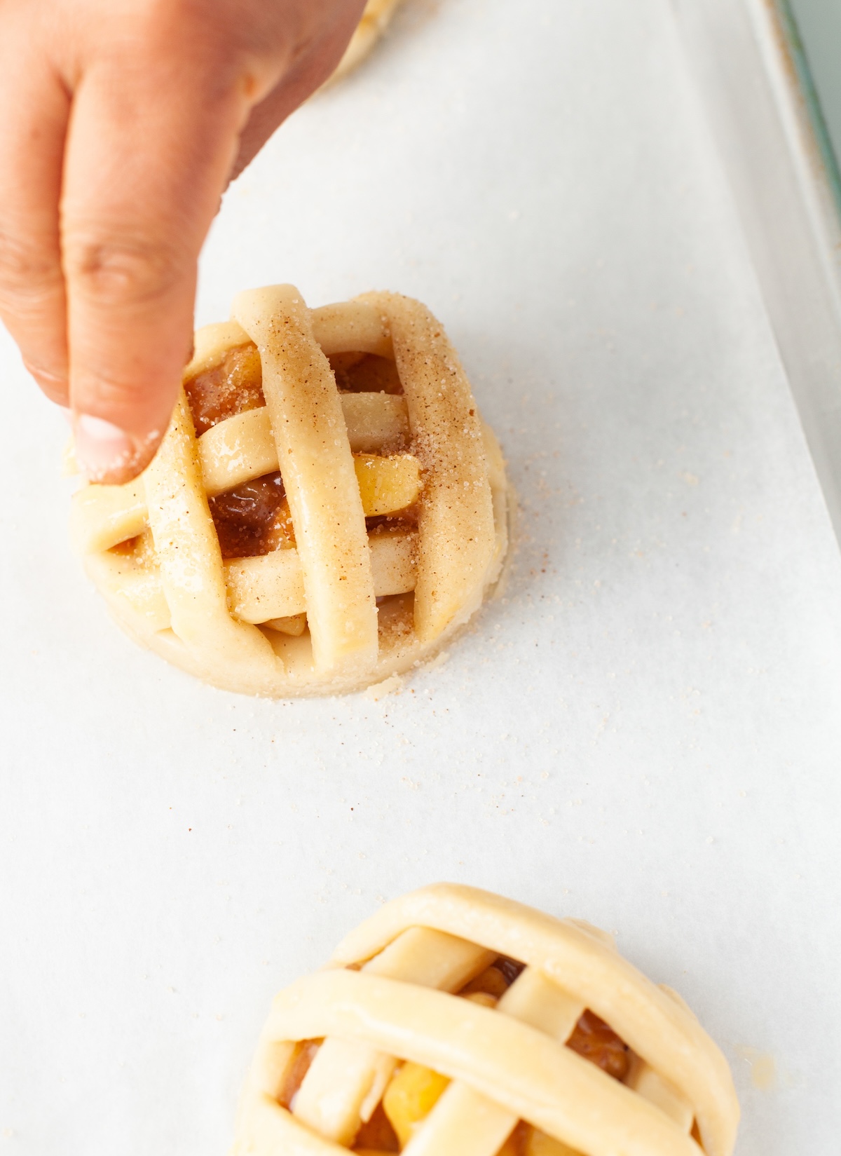 Sprinkling sugar and cinnamon on top of the mini pie cookies