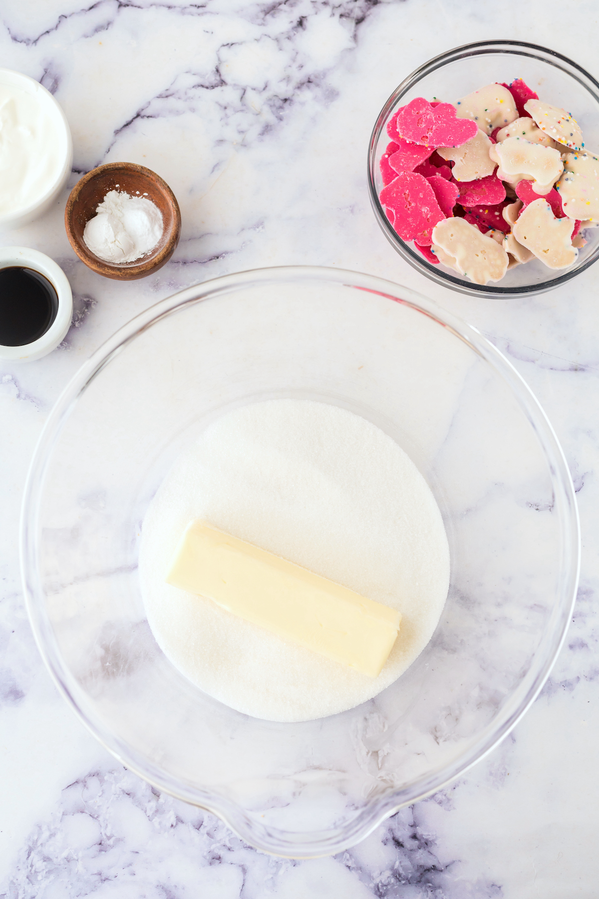 Butter and sugar in a clear glass bowl with animal cookies nearby